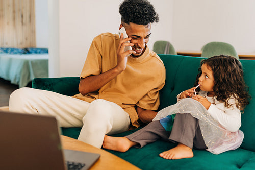 Smiling single father speaking on the phone while sitting with his daughter