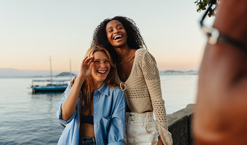 Two smiling young women enjoying a sunset by the sea