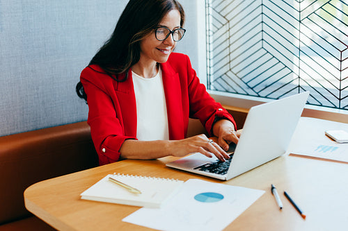 Businesswoman in red blazer working on laptop at office desk
