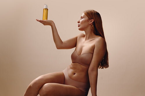 Woman holding skincare product bottle in minimalist beauty studio portrait