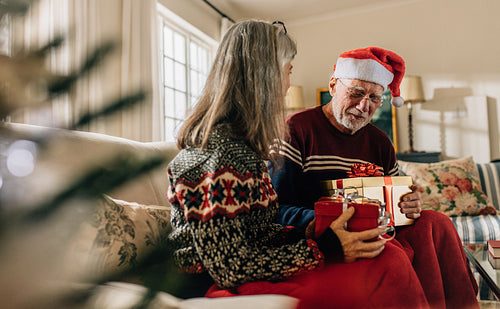 Senior couple exchanging christmas gifts sitting at home