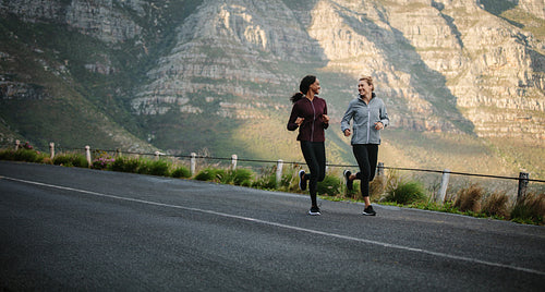 Two women athletes running on road