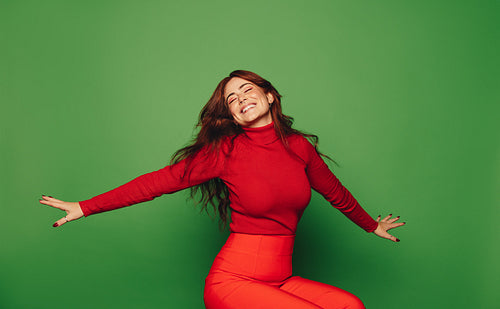 Young woman with carefree and vibrant style celebrating on green background with arms outstretched