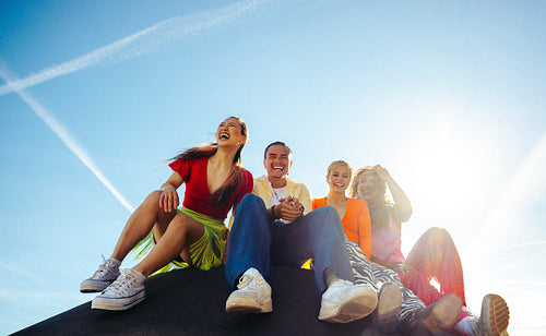 Sitting friends laugh together outdoors under a clear blue sky