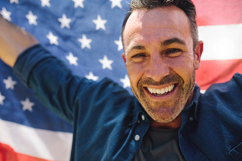 Close up of a smiling man holding american flag behind him