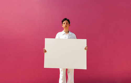 Young queer activist holding a white banner against a pink background