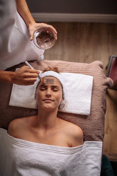 Cosmetician applying facial mask on female face