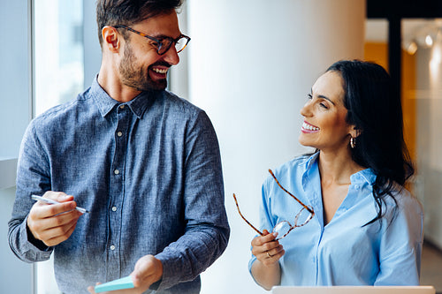 Two colleagues smiling and engaging in a friendly conversation at the workplace