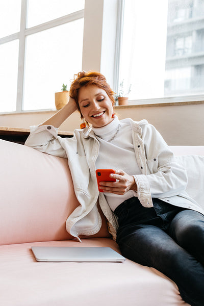 Smiling freelancer using smartphone on a couch in co-working space