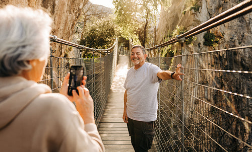 Elderly woman taking a picture of her husband on a bridge