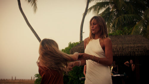 Happy mother and daughter dancing freely during a beautiful tropical sunset party