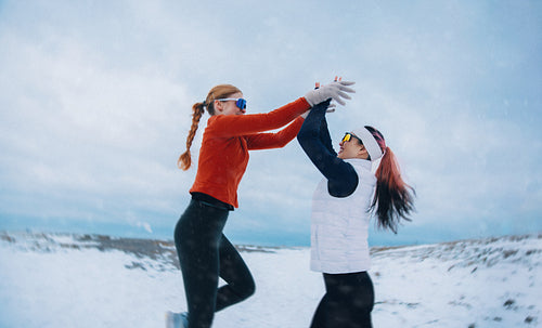 Women celebrating winter running achievement with a high five in the snow