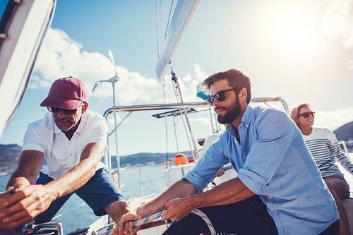 Father and son pulling rope to adjust sail on boat