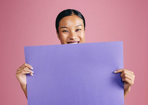 Woman with makeup holds a blank sign in a studio, smiling at the camera