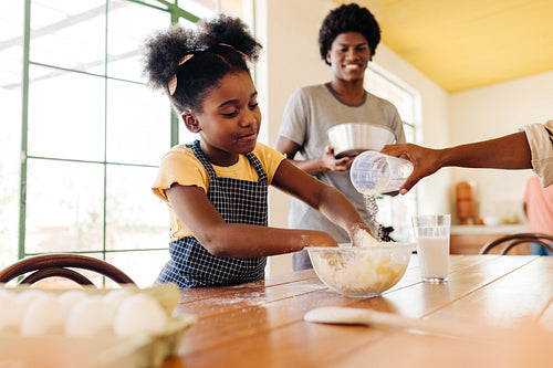 Family baking: Afro haired girl mixing dough for homemade bread in the kitchen