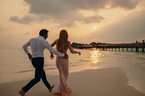 Island sunset joy: Playful couple running together on a sandy beach