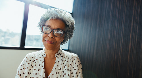 African business woman wearing glasses sits indoors near a window