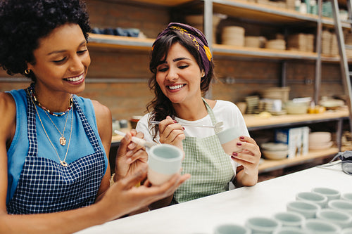 Happy young craftswomen decorating their handmade ceramic cups
