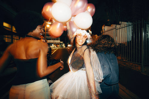 Group of girlfriends enjoying nighttime bachelorette celebration with balloons and fun outfits amid city lights