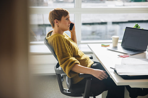 Woman sitting at her desk talking on mobile phone