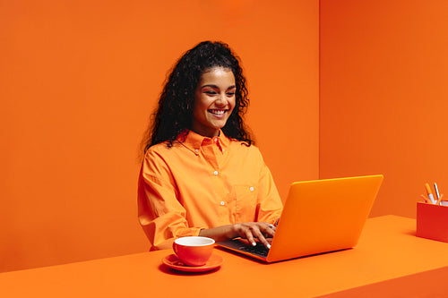 Monochromatic office concept with smiling African-American woman working on laptop with cup of coffee