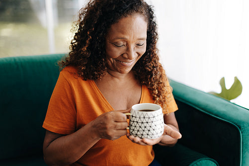 Elderly woman sitting on the couch and drinking coffee at home