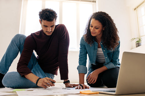 Business colleagues sitting on the floor and working with business papers spread on the floor