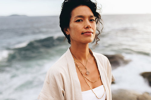 Woman wearing jewelry looking at camera on seaside during vacation at dusk