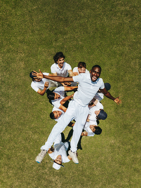 Team celebrating victory by lifting teammate on a cricket field