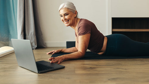 Happy senior woman browsing her laptop for online yoga classes at home