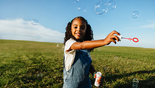 Playful outdoor child blowing bubbles in field with joyful smile