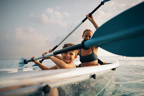 Mother and young son paddling a kayak together on a sunny ocean day