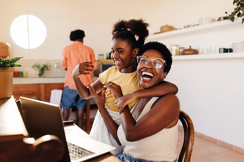Working mom laughing happily with her daughter while working from home