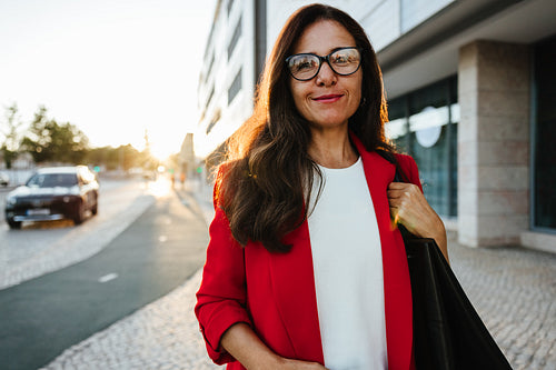 Smiling woman in red blazer standing outdoors during early morning sunlight
