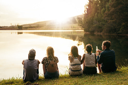 Young people sitting in a row by a lake