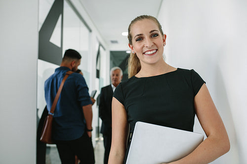 Happy woman in office corridor with coworkers at back