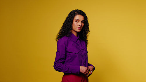 Confident woman in purple shirt and red pants poses against a vibrant yellow backdrop