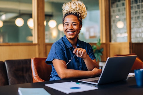Smiling young woman sitting at a desk with a laptop and papers