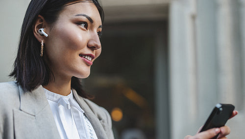 Asian business woman listening to music using a smartphone and earphones in the street