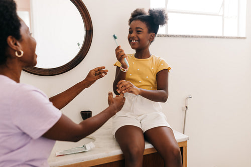 Happy mother guiding her daughter in brushing her teeth at the bathroom sink