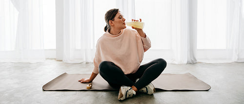 At home, the woman drinks after workout recovery on her yoga mat