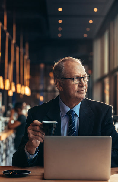 Senior business at cafe table with laptop drinking coffee