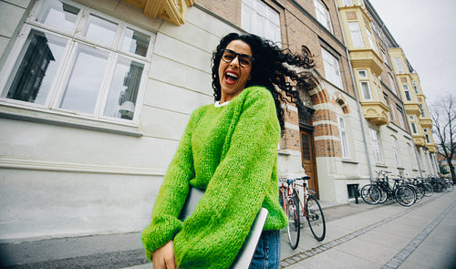 Smiling, the woman walks through the city with a laptop for work