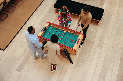 Overhead view of colleagues enjoying a foosball game in a modern office setting