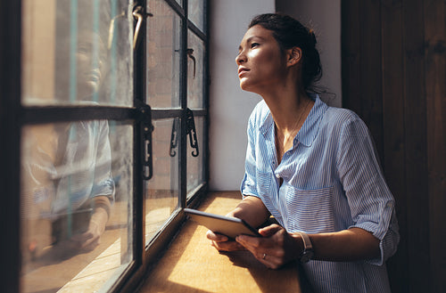 Woman standing by office window with digital tablet