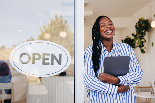 Cheerful young restaurant owner standing next to an open sign at the doorway of her new cafe