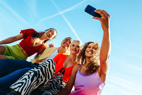 Diverse friends snap a selfie with a smartphone outdoors beneath clear blue sky