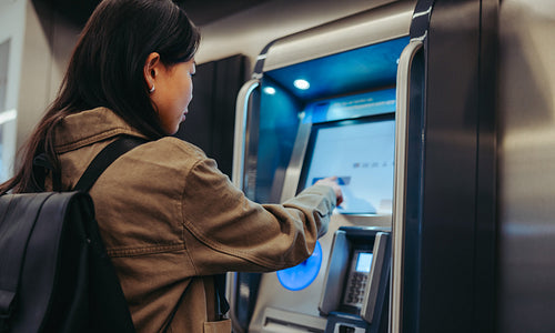 Young woman using ATM during city transit stop