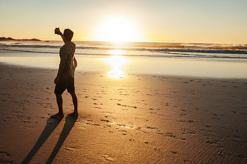 Young man taking selfie at sunset on beach