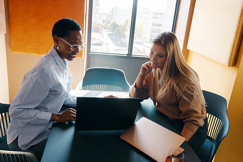Two women discussing project ideas at a table in a modern office